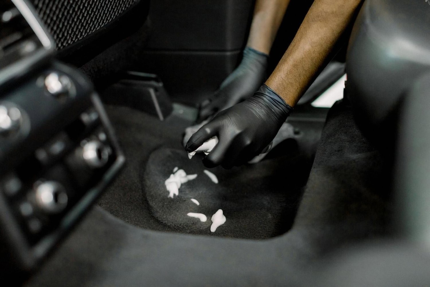 Gloved hand cleaning debris from a car floor carpet during a detailing session