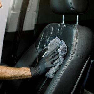 Detailer wiping down a black leather car seat during interior detailing in the UAE