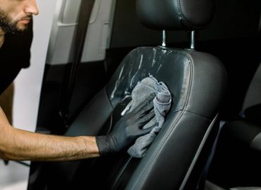 Detailer wiping down a black leather car seat during interior detailing in the UAE