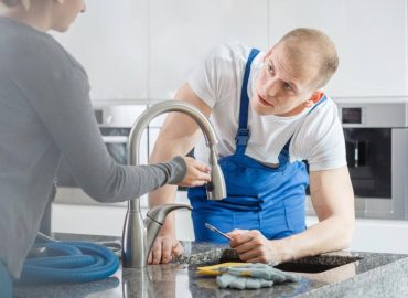 UAE plumber in blue overalls repairing a kitchen faucet for a homeowner