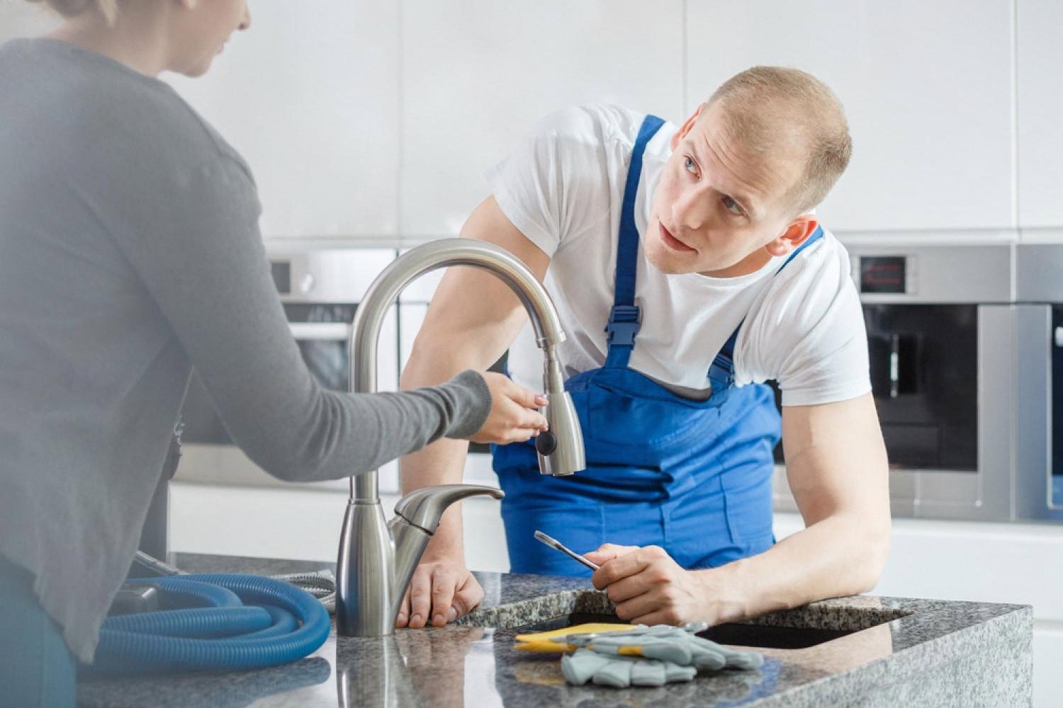 UAE plumber in blue overalls repairing a kitchen faucet for a homeowner