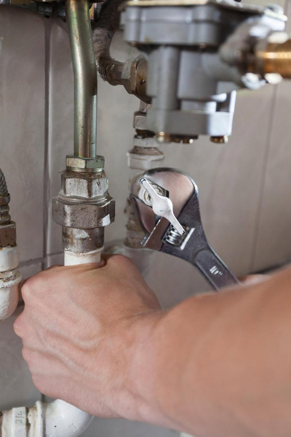 Plumber tightening a leaking under-sink pipe with an adjustable wrench